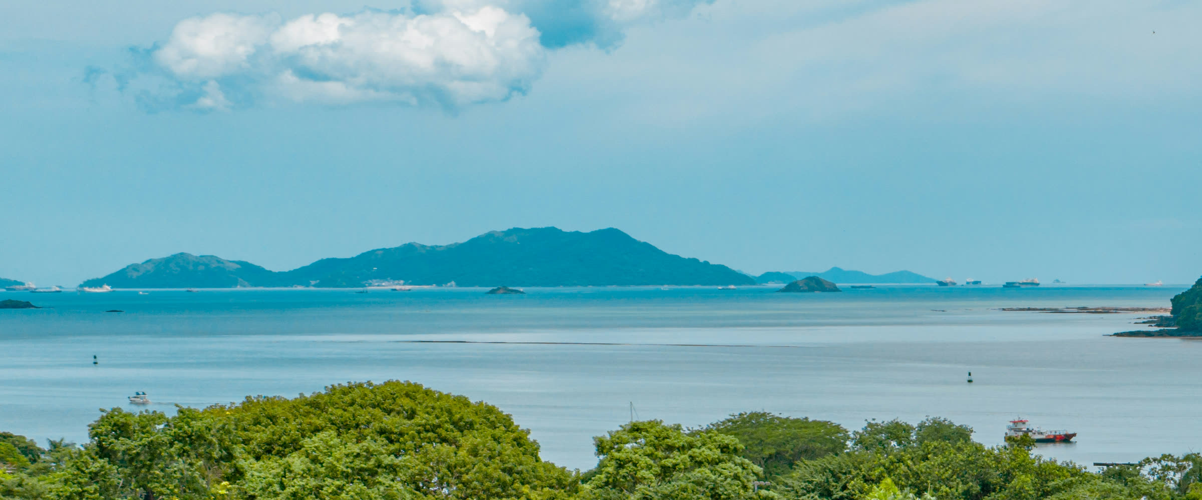 Islas montañosas en el horizonte de la bahía, con barcos fondeados y un islote rocoso